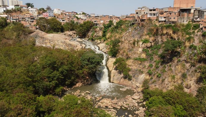 Cachoeira do Ribeirão Onça cercada por vegetação e moradias.